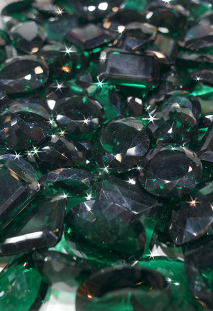 Many green gemstones are gathered closely together on a flat surface. They show several shapes and...