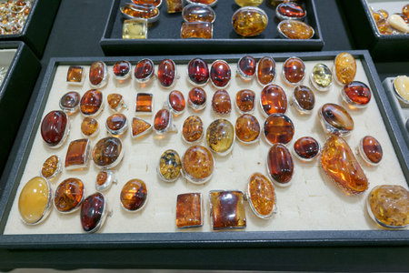 Amber stones in various shapes and sizes are arranged neatly in a display case. People walk around the market, browsing the jewelry on a sunny afternoon.の写真素材