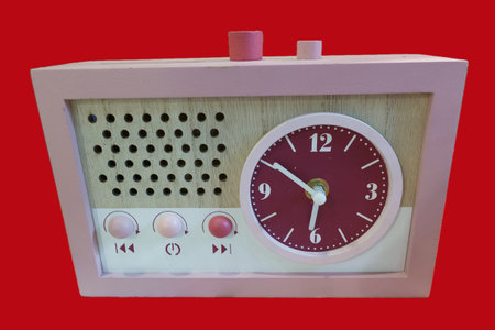A clock radio displays a round clock face with numbers and a speaker section. The device has buttons and is placed on a plain red background. It highlights a retro style.の写真素材