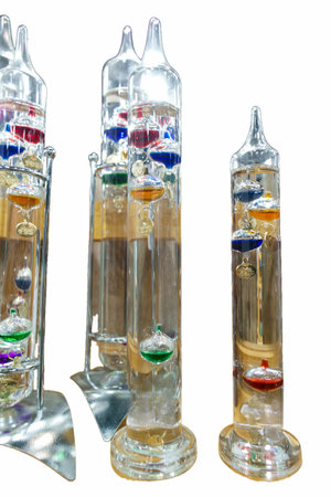 Several glass barometers stand in a row. Each barometer contains colored floating objects in clear...