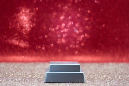 A small metallic block rests on a glittering surface. The background shows a red sparkly fabric that reflects light. This scene captures an everyday moment in a basic environment.
