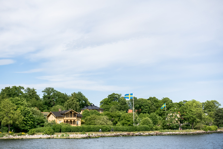 STOCKHOLM, SWEDEN - JUNE 6, 2016: Coastal houses with Swedish flags and cycling people, on an island of Stockholm archipelago, peaceful view on a sunny summer dayのeditorial素材