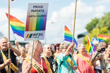 STOCKHOLM, SWEDEN â JULY 30, 2016: Woman holding a sign âProud parents of LGBT childrenâ in happy crowd waving rainbow flags during Stockholm Pride Parade on Hantverkargatan near the City Hallのeditorial素材