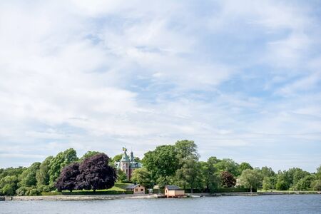 STOCKHOLM, SWEDEN - JUNE 6, 2016: Coastal view of an old small castle with Swedish flags on an island of Stockholm archipelago near Stockholm, viewed on a sunny summer dayのeditorial素材
