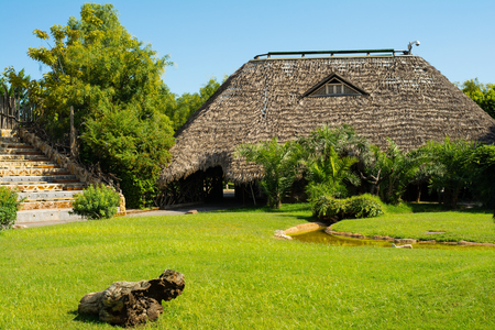 Relaxing view of green grass lawn and a rustic wooden house with straw roof in Valencia zoo, Spainのeditorial素材