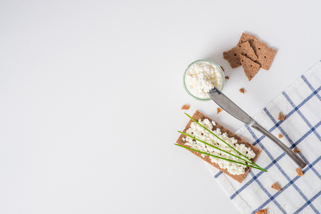 Brown rye crispy bread (Swedish crackers) with spread cottage cheese, decorated with thin green onion, on piece of cloth on white background with space for text, top view. Healthy snack conceptの写真素材