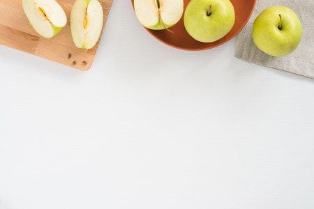 Fresh apples both whole and cut in pieces on wooden board, plate and cloth, on white background with copyspace, top view. Healthy food conceptの写真素材