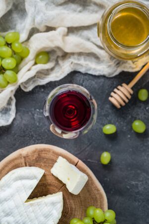 French soft cheese from Normandy region sliced on a wooden cut with green grapes, honey, spoon and...