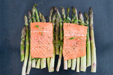 Two pieces of fillet of raw uncooked salmon on green asparagus on baking tray garnished with fresh thyme. Ingredients for lunch or dinner. Top viewの写真素材