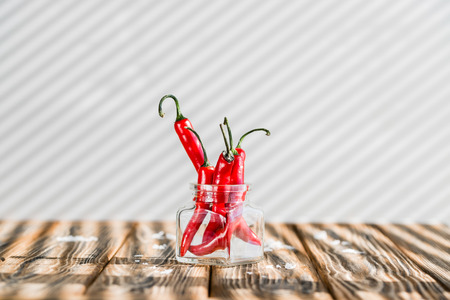 Red chili peppers in glass jar, sea salt and olive oil on wooden table. Harsh morning lightの写真素材
