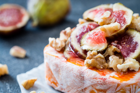Close up of raw French soft cheese from Brittany region covered with chopped figs, walnuts and honey on dark background. Snack conceptの写真素材