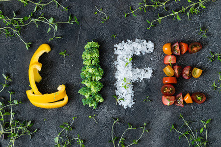 Inscription of fresh vegetables life on dark background. Letters made of pepper, broccoli, sea salt and cherry tomatoes garnished with thyme. Concept of healthy lifeの写真素材