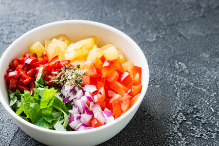 Freshly made mix of ingredients for salsa: pineapple, chili pepper, red onion, spices, mint. Mexican cuisine concept on dark backgroundの写真素材