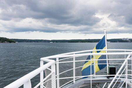 Swedish flag waving on a boat with a view over forests and water in the backgroundの写真素材