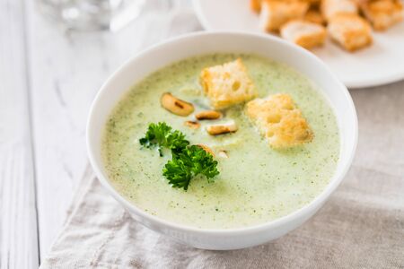 Green healthy cream soup with  broccoli, crackers, cashew, parsley. White wooden rustic background. Vegetarian breakfast conceptの写真素材
