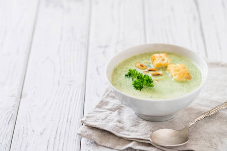 Green healthy cream soup with  broccoli, crackers, cashew, parsley. Copy space. White wooden rustic background. Vegetarian breakfast conceptの写真素材