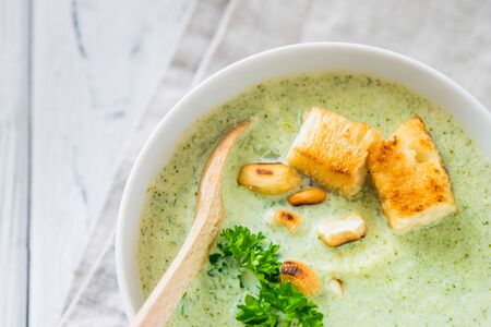 Green healthy cream soup with  broccoli, crackers, cashew, parsley. Top view on white wooden rustic backgroundの写真素材