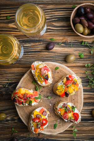 Traditional Italian appetizer, bruschetta with cottage cheese, cherry tomatoes, pepper, olives and fresh thyme, served with wine. Healthy snack concept on wooden rustic table. Top viewの写真素材