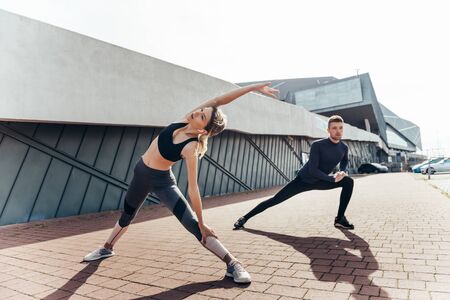Beautiful fitness sportgirl and sportmen with fit body in sportswear exercising outdoors, stretching, yoga, outdoor sports, urban style.の写真素材