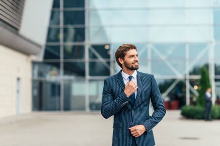 Confident businessman. Confident young man in full suit adjusting his sleeve and looking away while standing outdoors with cityscape in the backgroundの写真素材