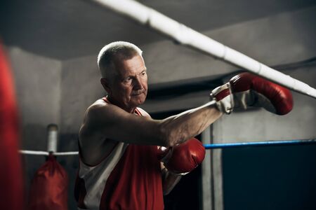 Old boxer practicing her punches at a boxing studio. Close up of a male boxer punching inside a boxing ringの写真素材