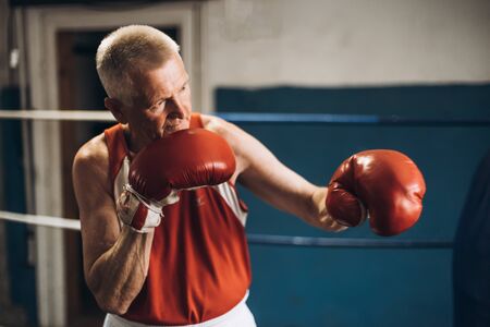Old boxer practicing her punches at a boxing studio. Close up of a male boxer punching inside a boxing ringの写真素材