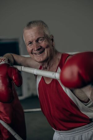 Happy funny senior boxer man with red gloves in the ring.