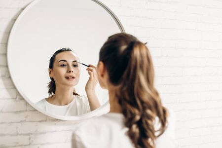 Beautiful young woman applying makeup in bathroomの写真素材