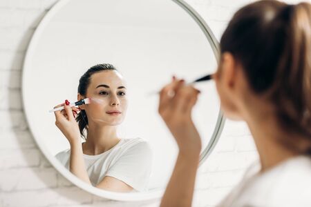 Beautiful female applying cosmetics on her faceの写真素材