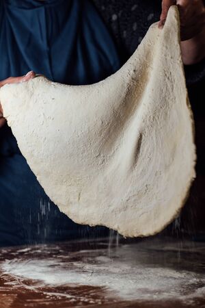 The wrinkled hands of a woman hold a rendered dough on a dark backgroundの写真素材