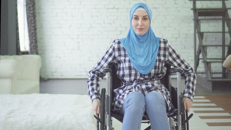 beautiful young woman in hijab disabled person, wheelchair, in apartmentの写真素材