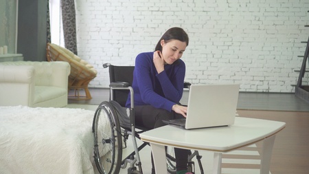 portrait of a smiling young beautiful disabled woman in a wheelchair, working at home on a laptop, remote work on the Internetの写真素材