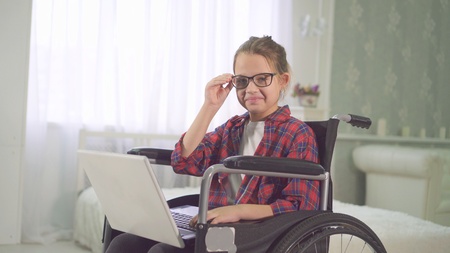 teenage disabled girl in a wheelchair using a laptop and looking at the camera smilingの写真素材