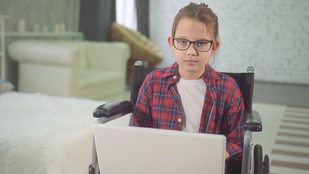 portrait of a disabled teenager in a wheelchair at home laptopの写真素材