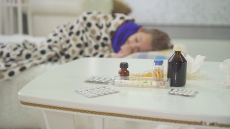 little girl is sick with a cold at home, there are pills and medicines in the backgroundの写真素材