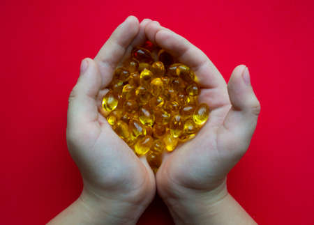 Omega 3, yellow transparent fish oil capsules in the hands of a child.の写真素材
