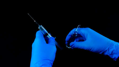 Hands in blue gloves, a syringe in one hand, an ampoule in the other.