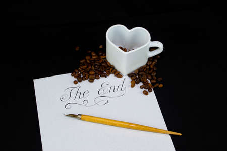 A white heart-shaped mug with coffee beans on a white sheet has the inscription end and the pen pen lies at the bottom of the inscription.の写真素材