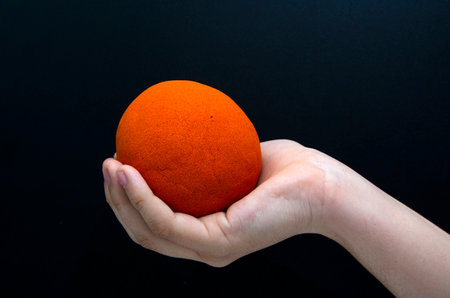 Orange ball in hand on a black background.の写真素材