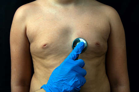 A doctor in blue medical gloves listens to the boy with a stethoscope.の写真素材