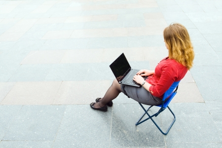 Image of the businesswoman sitting and using the laptop in the empty street. Focus is made on top of the background marbled tile in the street.の写真素材