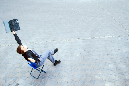 The image on top of a businessman sitting in the street, which works with the computer and has a success.の写真素材