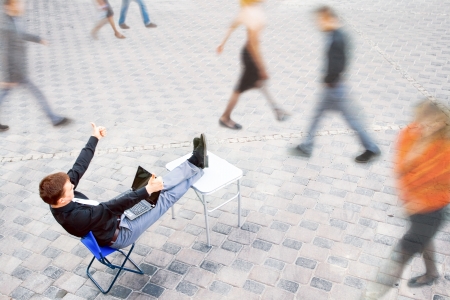 The image on top of a businessman sitting at the table in the street, which works with the computer and has a success.の写真素材
