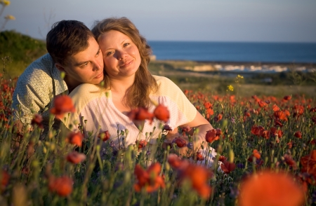 Portrait of beautiful couple young women and young man in flowers, poppy, seaの写真素材