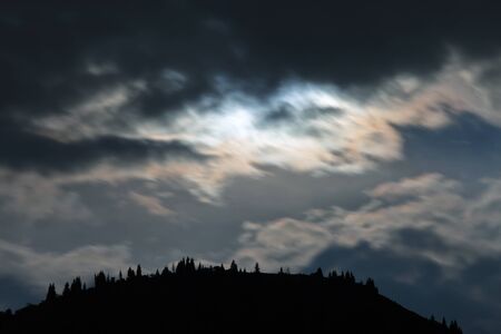 Night scenery of clouds, illuminated by the moon with the silhouette of trees and mountains, Almaty.の写真素材