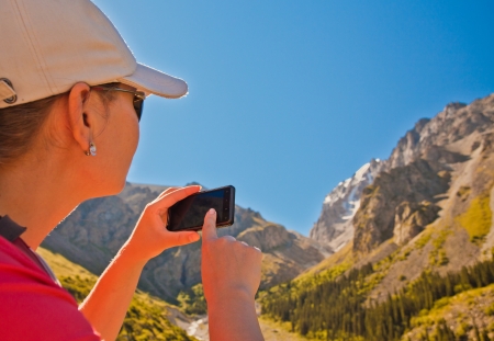 Image of a young girl using her mobile against a background of beautiful mountain scenery of Ala-Archa, Kyrgyzstan.の写真素材