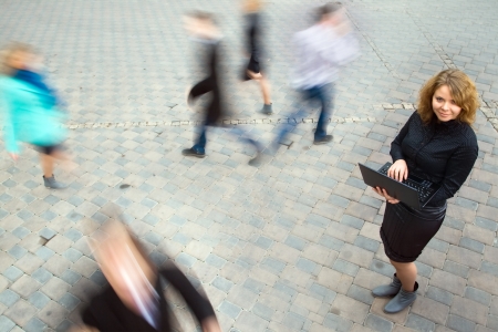 Young attractive businesswoman working on laptop through wireless technology. Motion blurred commuters walking to workの写真素材