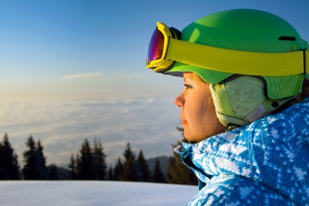 Portrait of a young woman, who snowboarding in the snowy mountains looking the sunset. In the background clouds, illuminated by all shades of the sunset after a bright sunny winter day.の写真素材