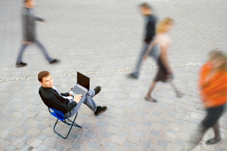 The image of a businessman working on the computer and sitting in the middle of people at the streetの写真素材