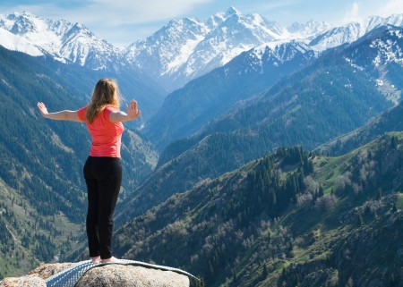 The young woman is doing yoga warm-up before the yoga asanas on the summit. On the background is a range of high tops of mountains.の写真素材